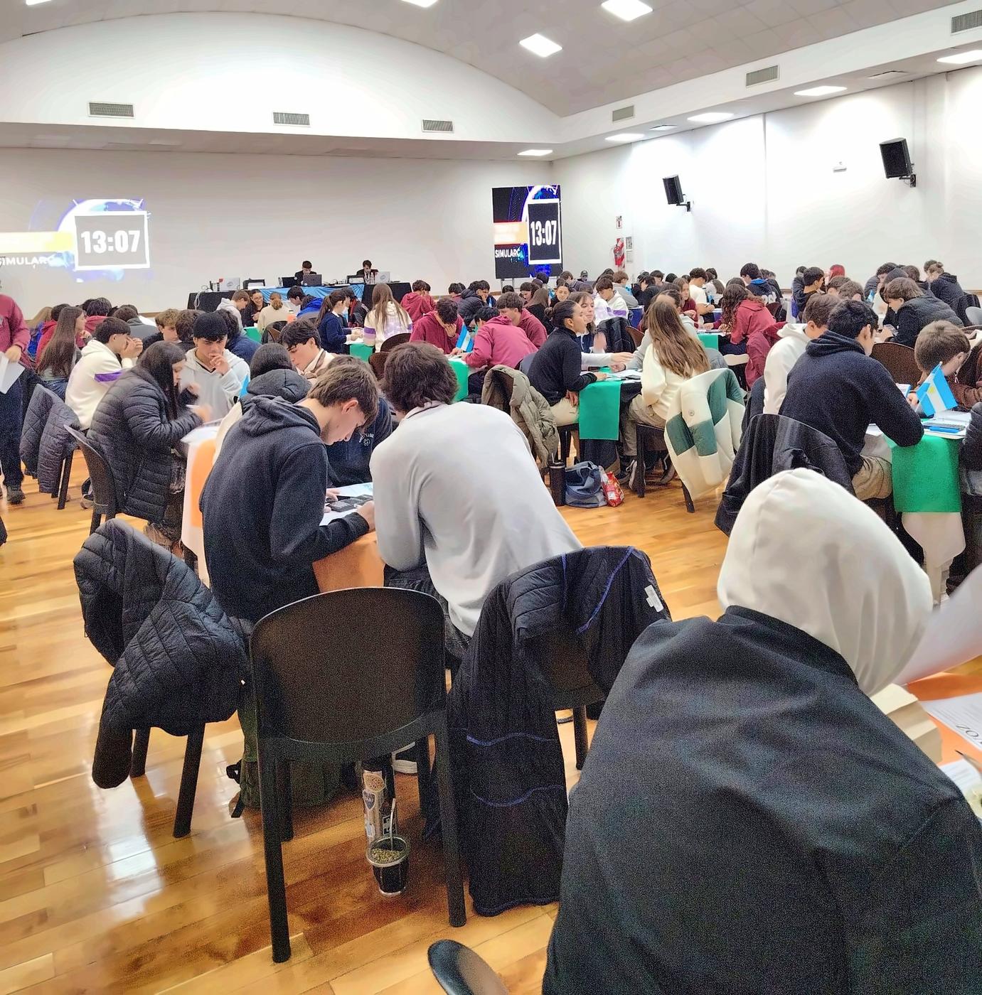 Salón colmado de equipos durante una ronda, con la cuenta regresiva del tiempo de entrega en las pantallas