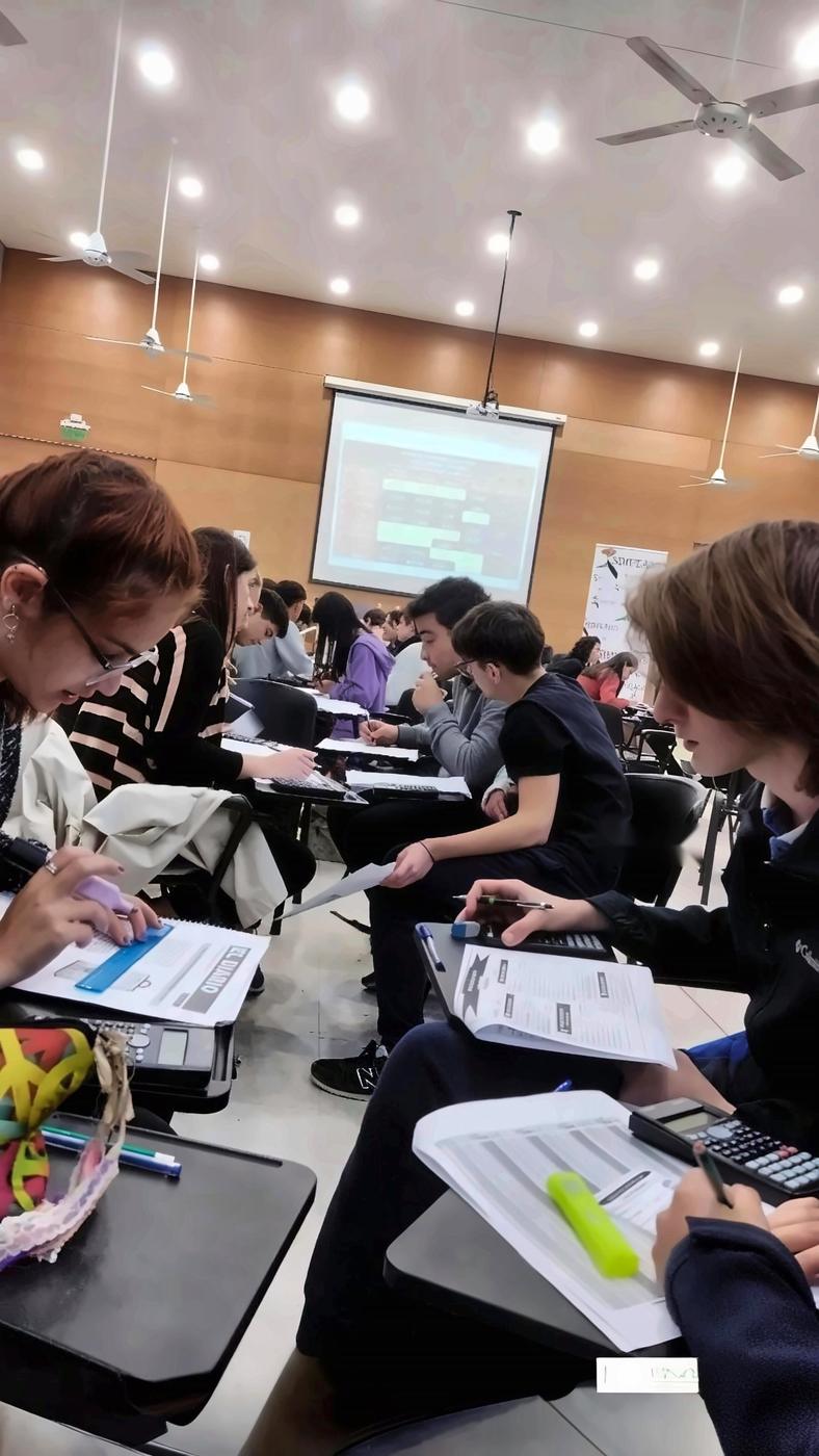Estudiantes completando sus hojas de trabajo en un auditorio, con los resultados proyectados al fondo